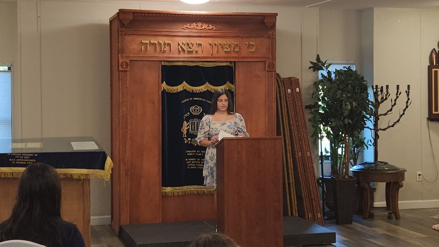 A bat mitzvah girl reading from the podium in front of the ark at Chabad of Venice