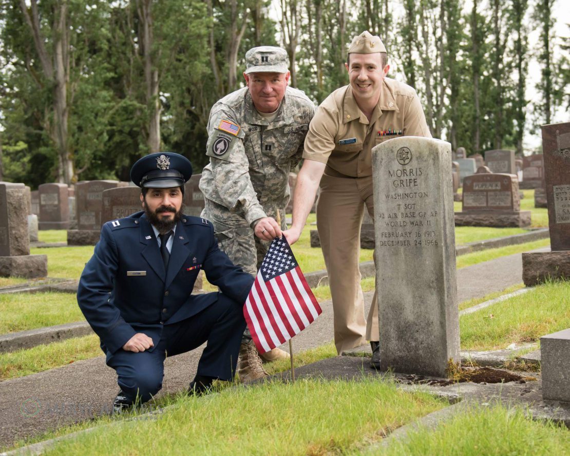 Military chaplains in uniform placing an American flag at a veteran's grave