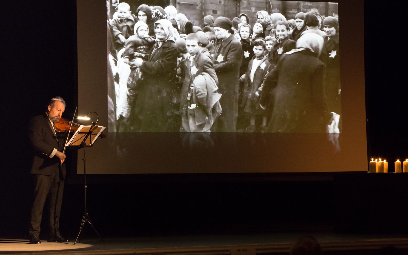 Violinist Vladimir Tsypin performing on stage before a projected archival photograph