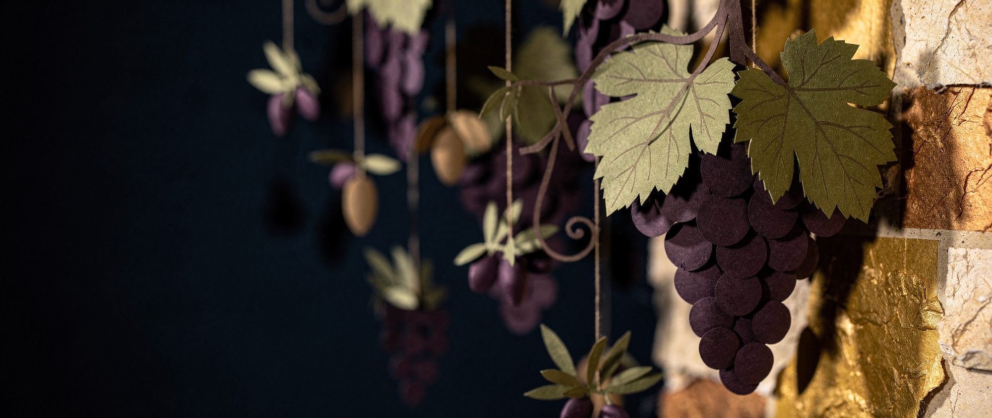 Papercut cluster of ripe grapes hanging from a vine against warm Jerusalem stone