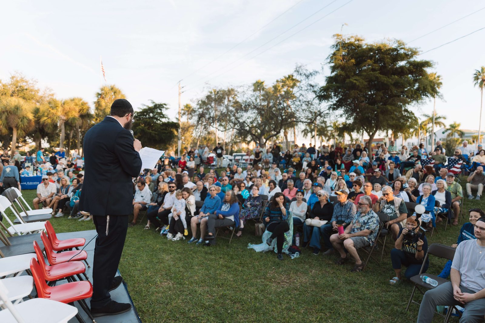 Rabbi Sholom Schmerling addressing a large community crowd at an outdoor gathering