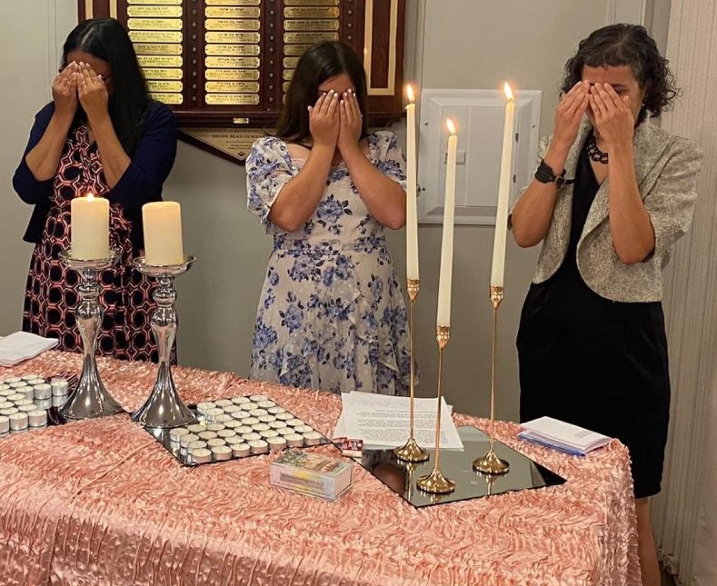 Women covering their eyes over freshly lit Shabbat candles